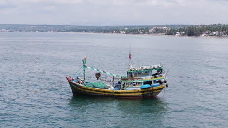 Fisherman-boat-in-front-of-Centara-Resort-in-Mui-Ne,-Vietnam,-aerial-parallax-shot