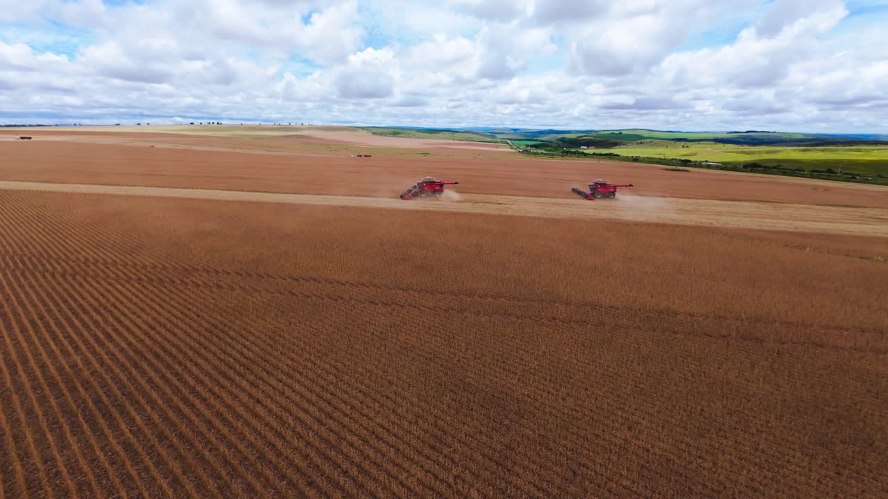 Aerial view capturing combine harvesters working on a vast soy plantation in sunny São João da Aliança, Goiás, Brazil, with scattered clouds enhancing the landscape