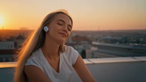 Woman Enjoying Music with Earbuds on a Rooftop at Sunset