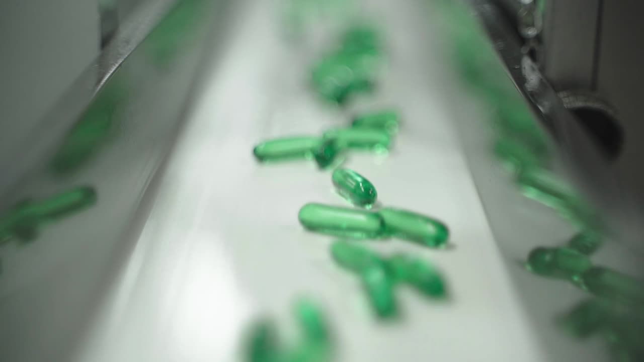 Green capsules moving for packaging on fast conveyor in pill plant.
