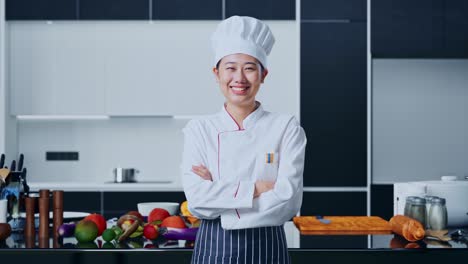 mujer chef asiática sonriendo y cruzando los brazos a la cámara en la cocina de casa