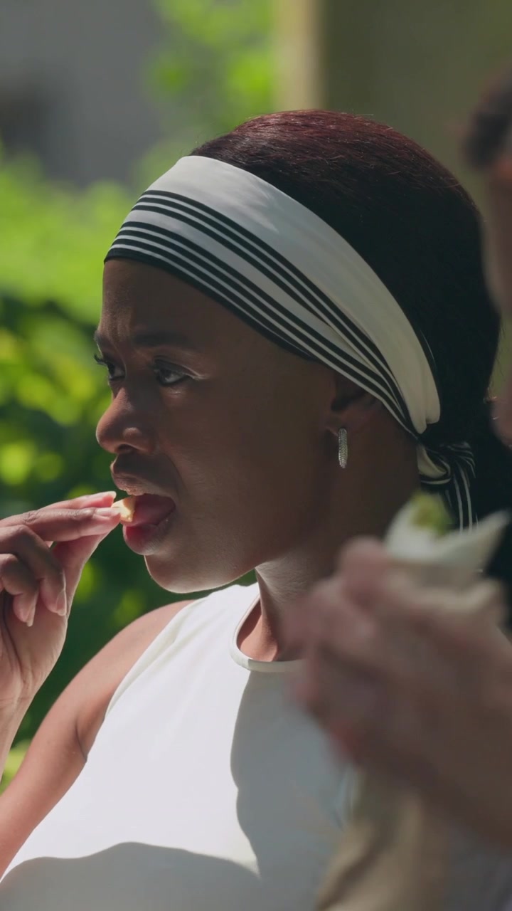 Vertical video: Camera widening, right woman eating cone while left mouthing to chat, with headband