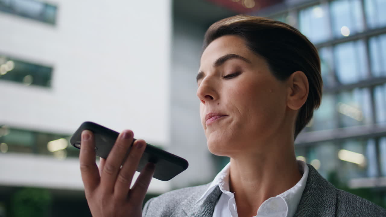 Company executive recording voice message on smartphone. Serious woman send mail