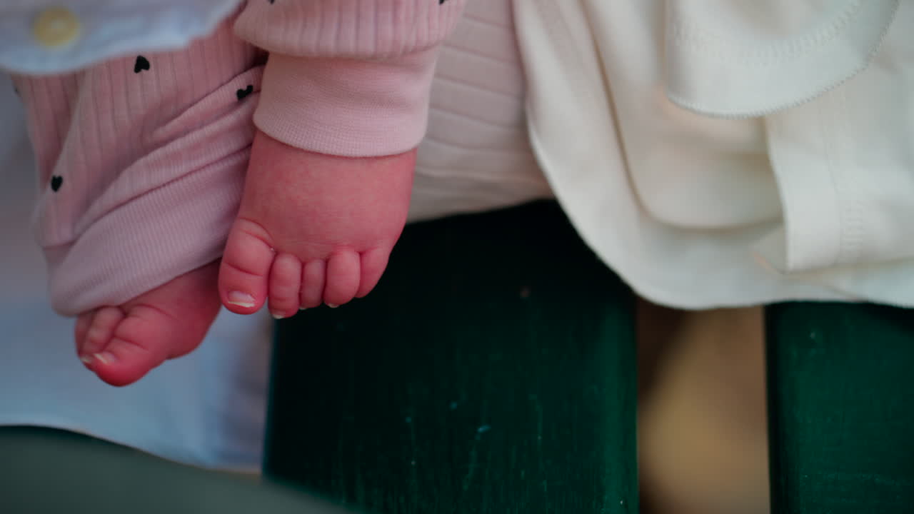 Close up shot of a baby's feet resting on a bench, wearing soft pink clothes with small heart patterns