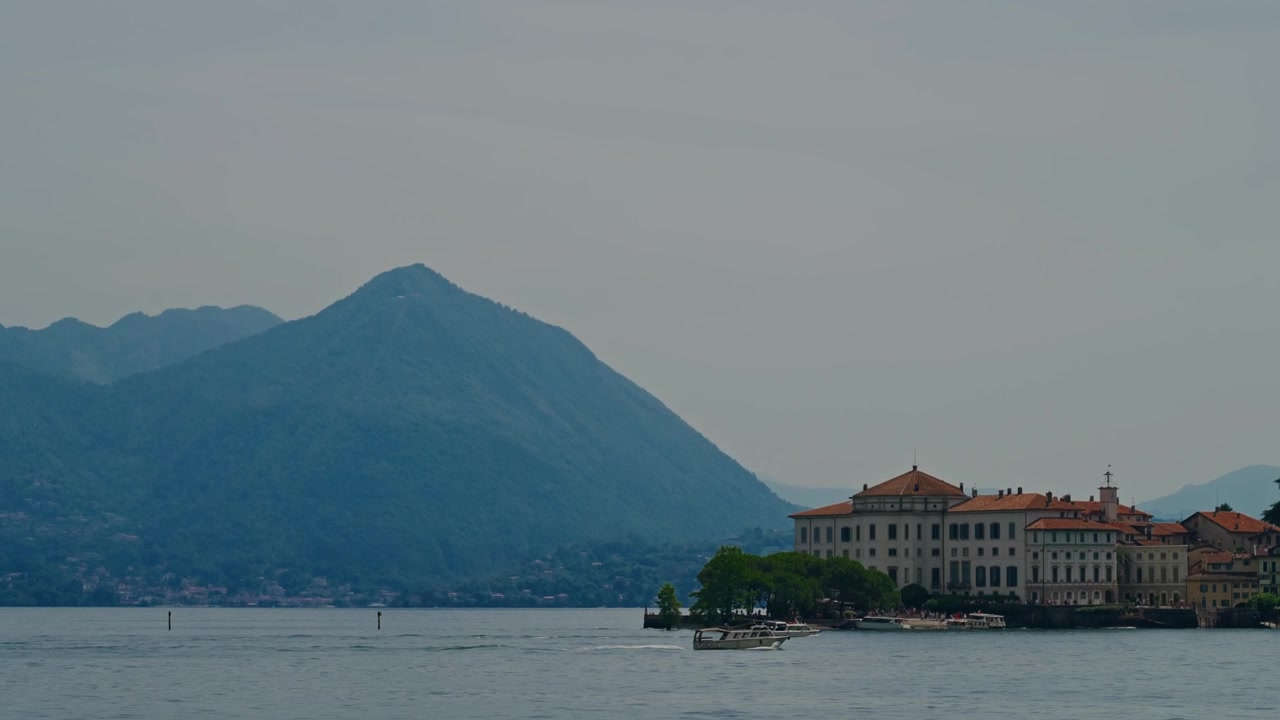 Piccole barche navigano sul lago di fronte alle Isole Borromee con maestose montagne sullo sfondo, catturando la bellezza e la tranquillità del nord Italia.