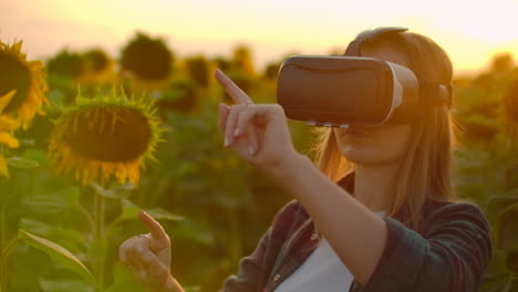 the woman with long hair in plaid shirt and jeans is working in vr glasses. she is engaged in the working process. it is a great sunny evening in the sunflower field at sunset.