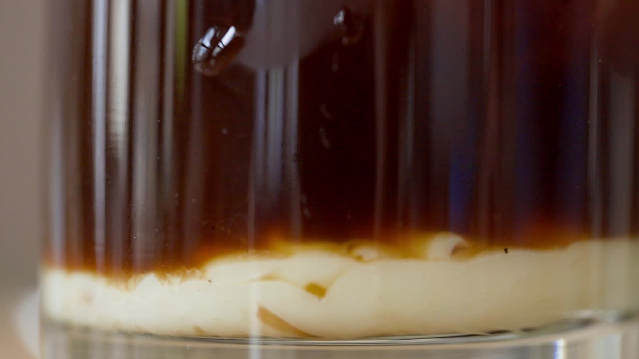 Condensed milk poured into black coffee in glass
