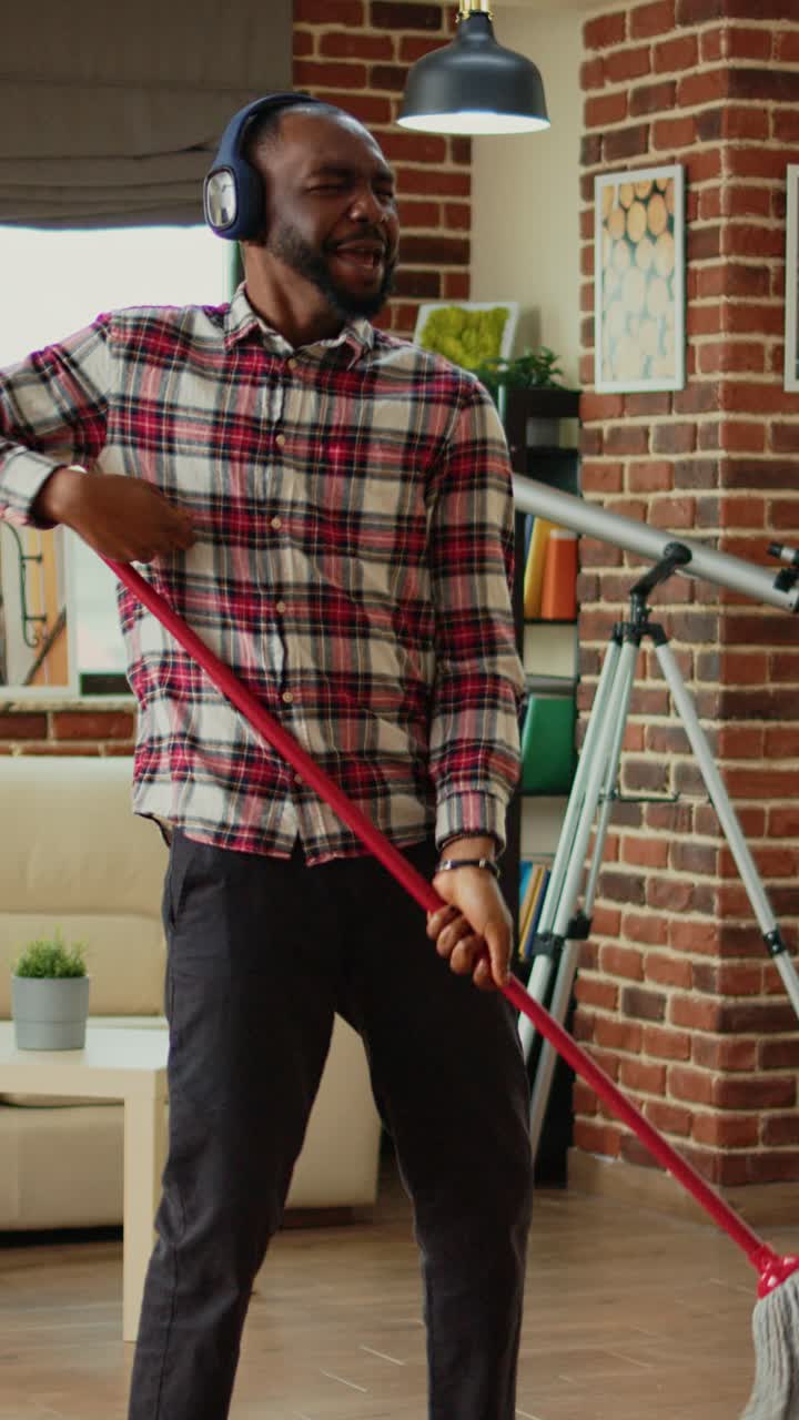 Vertical video: African american person using mop to wash wooden floors