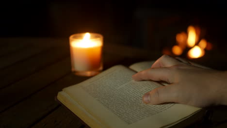 a man reading an old antique book by a cosy fire and lit by candlelight close up