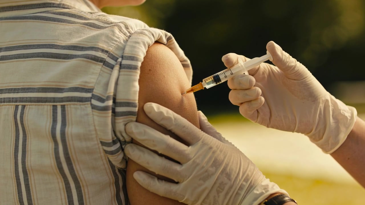 Steadying gloved worker inserting syringe into teen's arm at park, giving vaccine, striped top