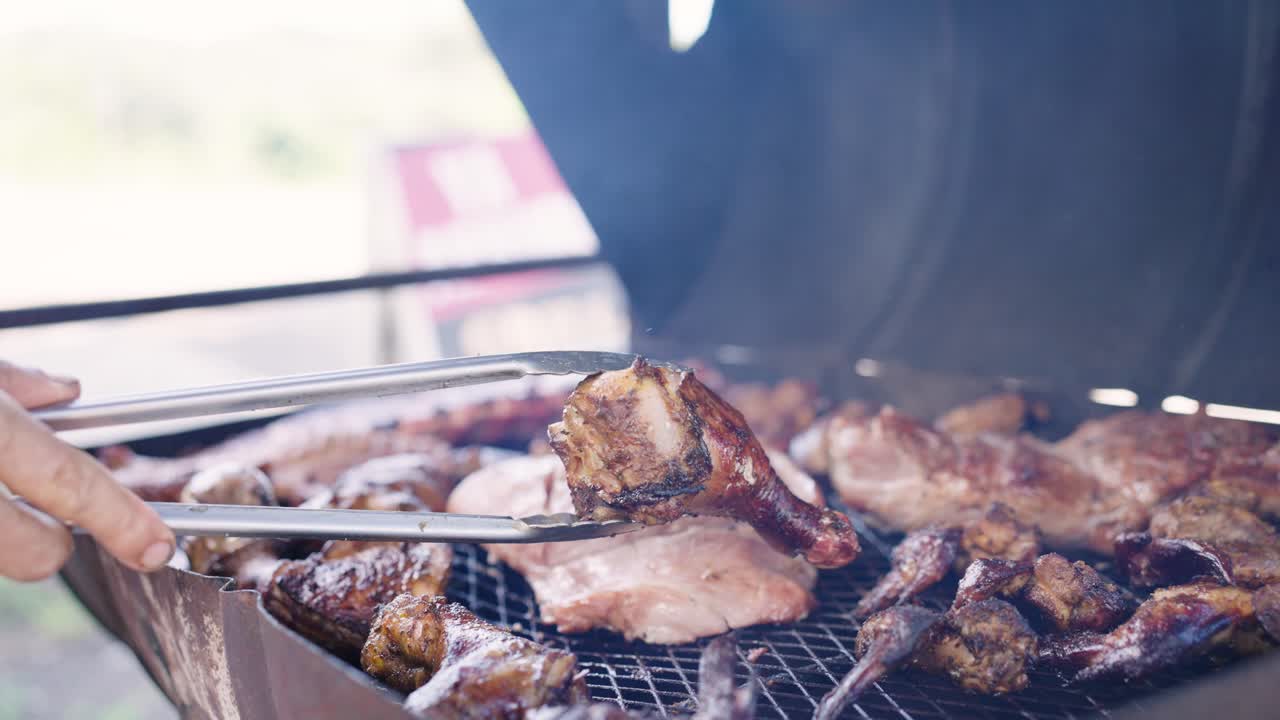Una mano che gira grandi tagli di carne e pollo su una griglia da barbecue all'aperto.