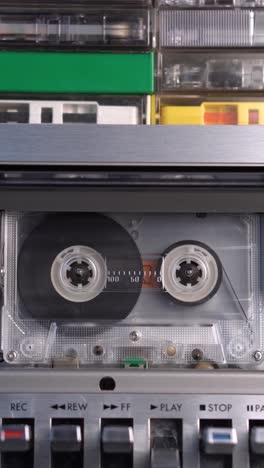 vertical view of audio cassette tape playing in deck with bunch of cassettes on top, vintage recordings from 1970s and 1980s