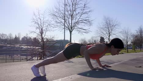 joven atlética haciendo flexiones en la acera con sol brillante detrás
