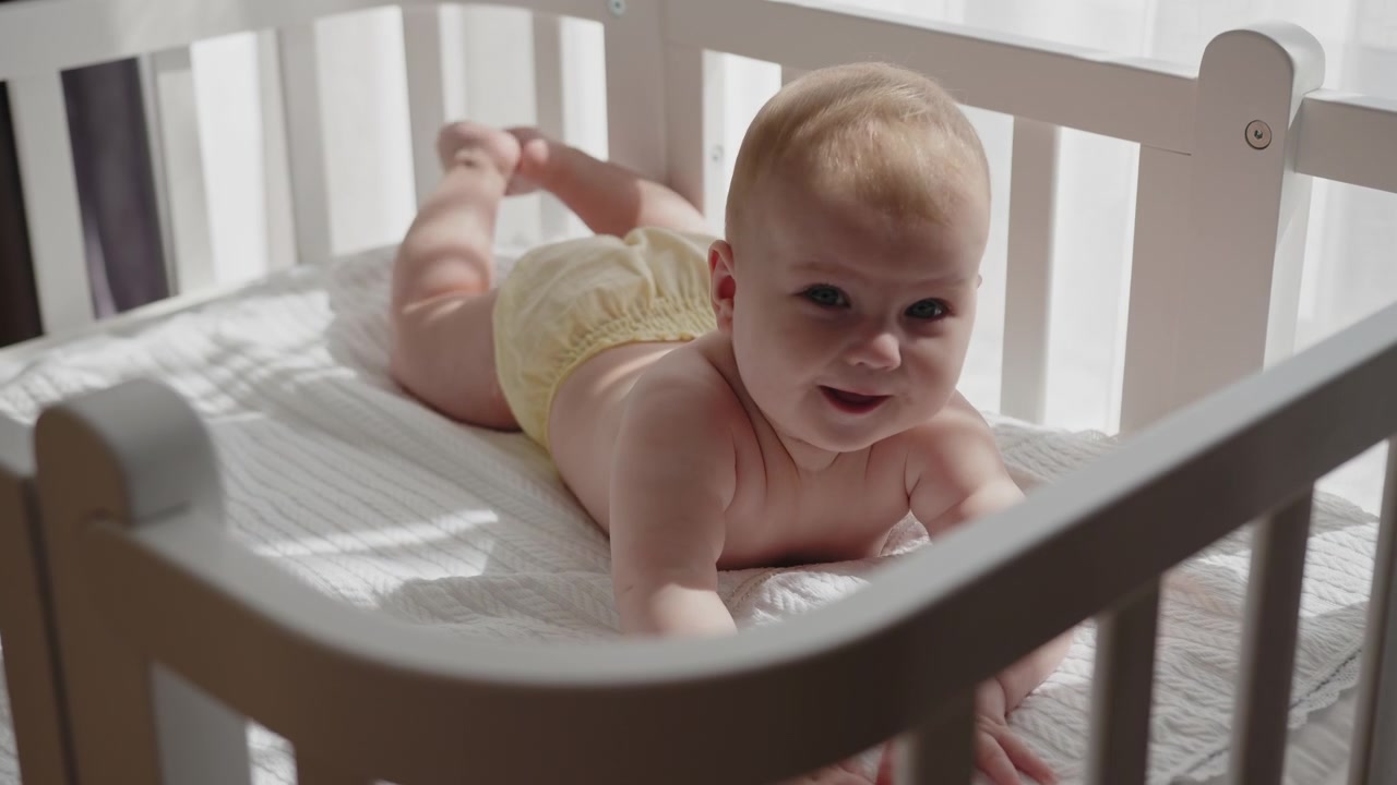 Closeup of infant on stomach in crib looking towards camera with bright eyes bathed in soft sunlight