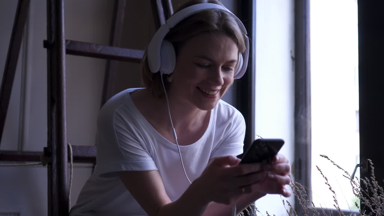 chica sonriente con auriculares enviando mensajes de texto en el teléfono
