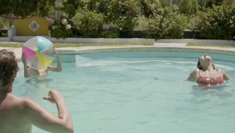 familia caucásica jugando a la pelota en la piscina en un día de verano