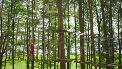 cute girl dressed in pink climbing in adventure park in forest during summer