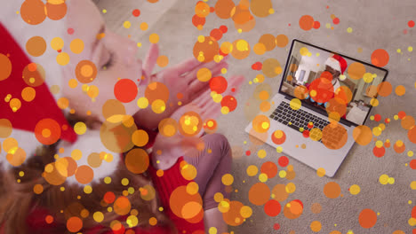 Animation-of-light-spots-over-caucasian-woman-in-santa-hat-on-laptop-video-call-at-christmas