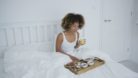 frau mit smartphone im bett beim essen