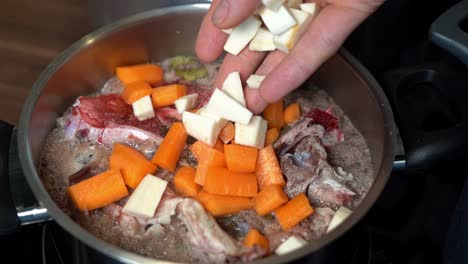 person adding chopped parsnips to bone broth beginning to boil in pot