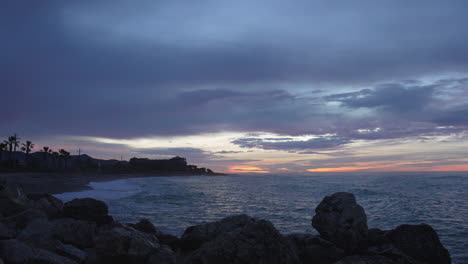 nightfall beach bay man enjoys his time looking at sunset, sits on rocks