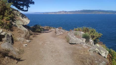 wooded trail along the mountainside with the cliff and the sea, the coast in the background, sunny summer day, shooting traveling forward, cíes island, pontevedra, galicia, spain