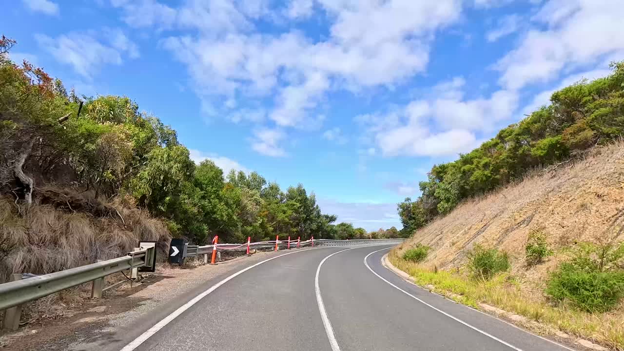 A 14-second video captures a winding road through lush greenery and coastal views under a bright blue sky