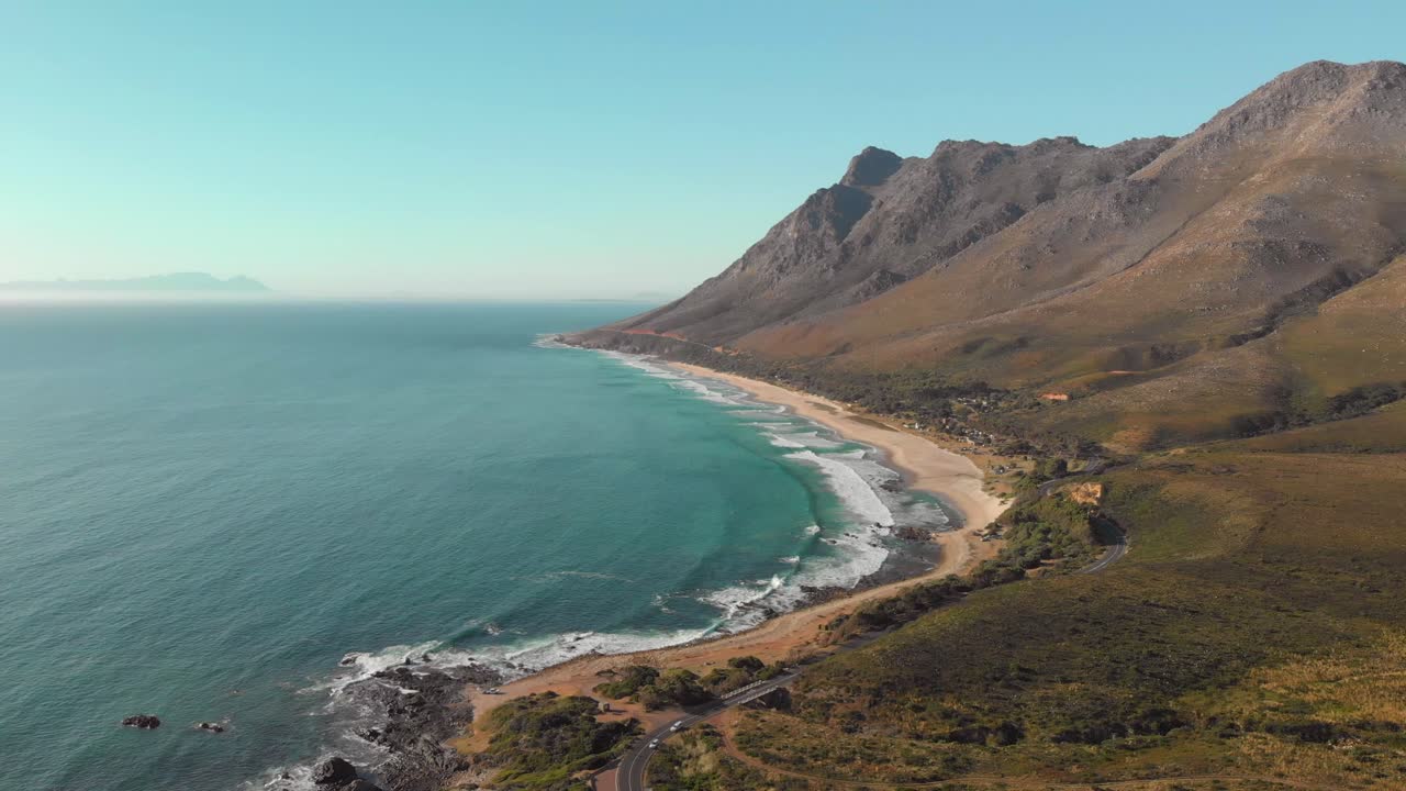 Static aerial drone view of coast line with mountain range, road, beach and sea