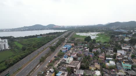 Toma-De-Drone-De-Una-Carretera-Cerca-De-Un-Lago-Rodeado-De-Edificios-Y-Colinas-Al-Fondo.