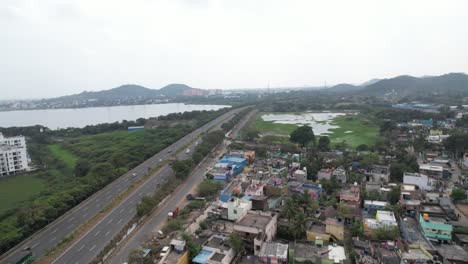 drone shot of highway near a lake surrounded by buildings and hills in the background