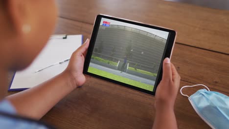 composite of woman sitting at table with face mask, watching athletics javelin event on tablet