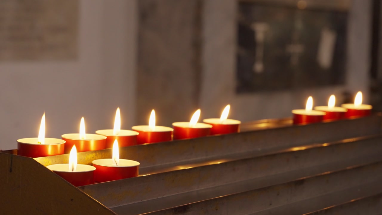 Votive candles on altar in church or cathedral in European city burning light and flame in honor or in memory or prayer. Spiritual christian tradition. Catholic church burning red candle lit dark room