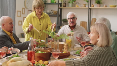 senior woman putting salad for guests at home dinner party