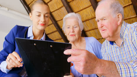 Low-angle-view-of-Caucasian-senior-couple-discussing-over-clipboard-with-female-doctor-at-comfortabl