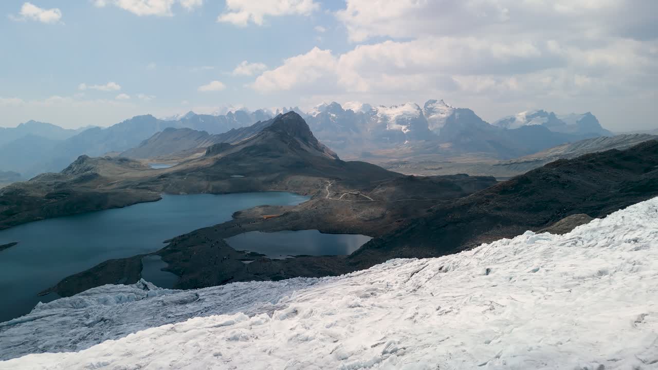 A beautiful, slow aerial shot descends over the edge of the vast Pastoruri Glacier, revealing the stunning high-altitude landscape of the Peruvian Andes with several alpine lakes below