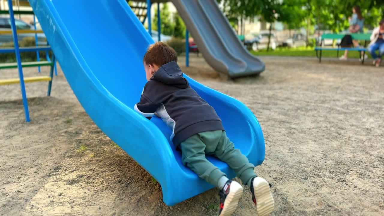 Little boy wants to climb by the slide on the playground. Kid fails every time but doesn't stop trying.