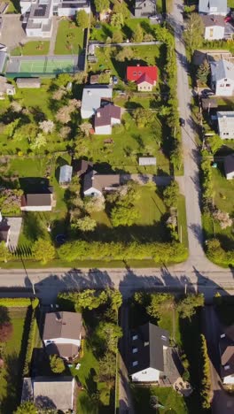 katlakalns neighborhood gardens, fenced plots, and houses with intersecting streets and long tree shadows cast on the asphalt under afternoon sun, aerial view, vertical pull out drone shot