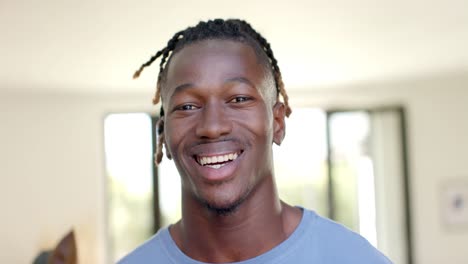 portrait of happy african american man with short dreadlocks at home smiling, in slow motion