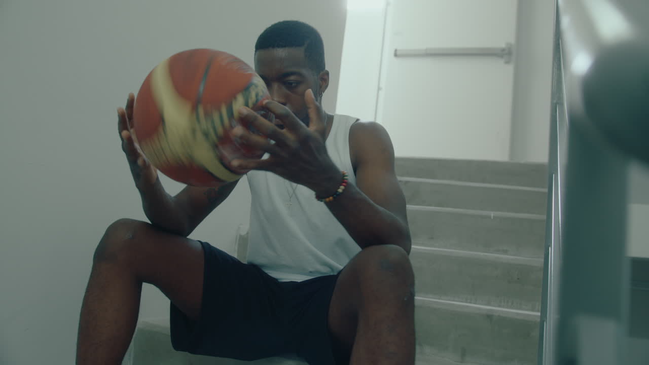 Sort atlet sidder på trappen og håndterer en basketball.