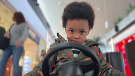 surprised two-year-old black baby, mix raced, driving a remote controlled toy car inside a mall