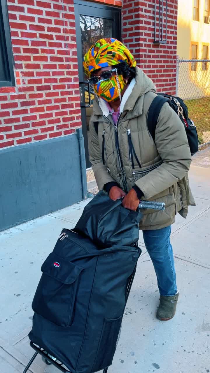 New York, USA, 11 May 2025: Person with colorful headwrap pushing shopping cart on sidewalk