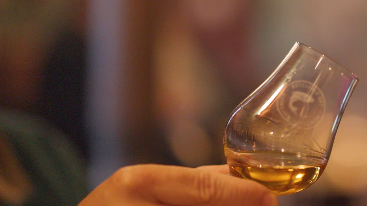 Hand swirling whisky glass in warm, cozy bar with amber reflections and softly blurred background