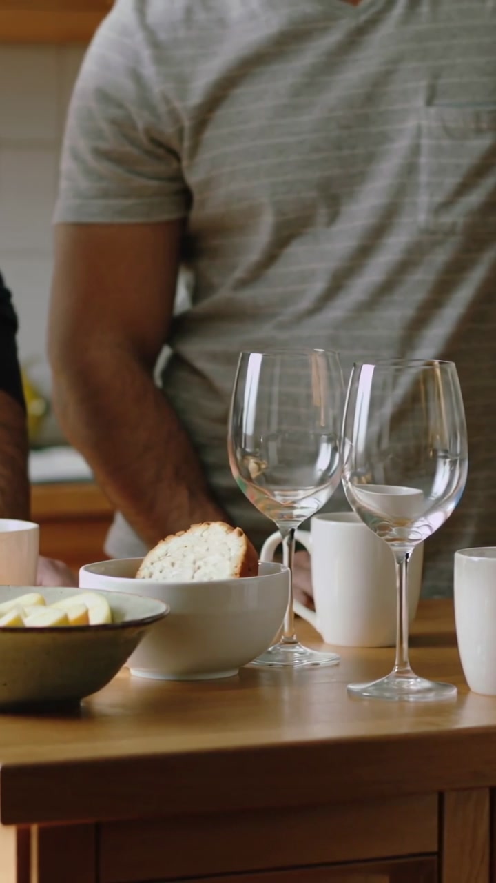 Vertical video: Hand coming right, reaching mug at kitchen island, man gray shirt arranging glasses
