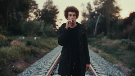 young man smoking on train tracks