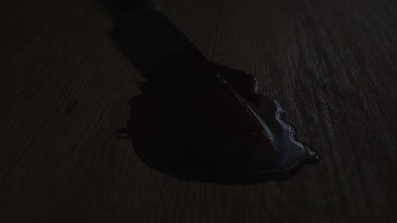 Filmatisk kamerakjøring av en blodig kniv i en blodpøl på et grusomt åsted med politilys som blinker i bakgrunnen.