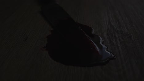 cinematic dolly of a blood covered knife in a pool of blood on a grizzly crime scene with police lights flashing in the background