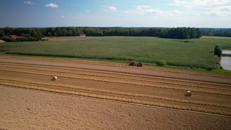 aerial parallax around tractor and hay bales on empty dry agriculture fields, blue sky