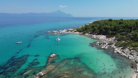 La-Gente-Nada-En-El-Mar-Azul-Claro-En-La-Bahía-De-Orange-Beach-En-Halkidiki,-Grecia---Antena-4k