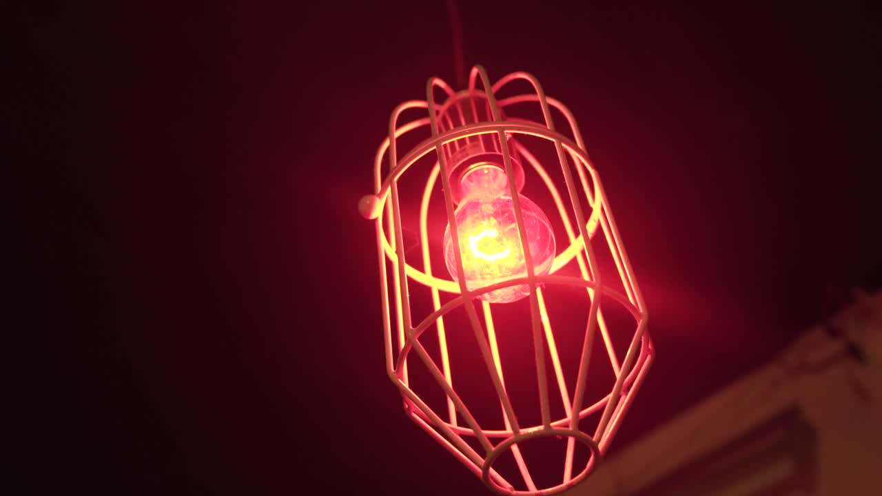 A Red Light Bulb With Wooden Cage Hanging At The Ceiling - low angle shot