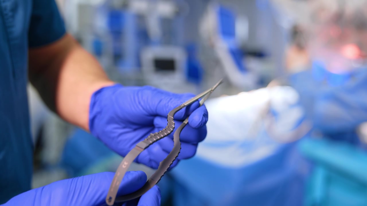 Médico con guantes de látex azules sostiene una herramienta médica metálica moderna. Primer plano. Instrumental para neurocirugía.